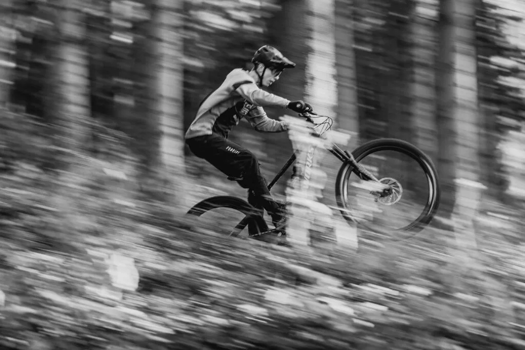 Mountain biker riding fast through a forest trail, showcasing control and performance
